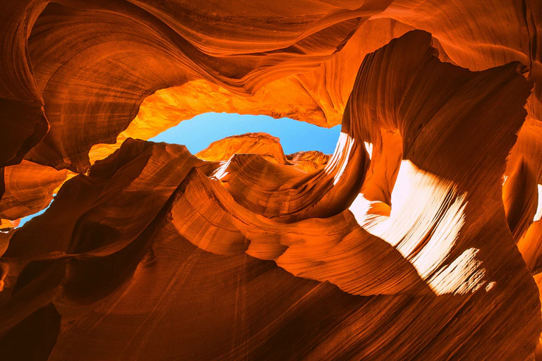 Orange sandstone walls framing blue sky inside Antelope Canyon